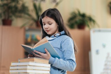 Öğrenci kız kitabına derinden odaklanmıştı. Parlak bir sınıftaki ders kitaplarının arasında duruyordu. Bilginin ve keşfin neşesini somutlaştırıyordu..