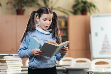 Canlı bir sınıf ortamında, liseli bir kız bir kitaptan okurken neşesini ifade eder. Yüksek kitap yığınlarıyla çevrelenmiş, öğrenme hevesiyle sınıf arkadaşlarını büyülüyor..