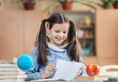 Mutlu bir liseli kız bir masada oturur, defterine kurşun kalemle yazar. Etrafı kitaplar, bir elma ve bir küre ile çevrili, neşeli bir sınıfta ders çalışmaktan zevk alıyor..