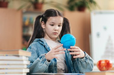 Liseli bir kız, etrafı kitaplarla ve elmalarla çevrili parlak mavi bir küreyle meşgul oluyor. Canlı bir sınıf ortamında öğrenme hevesini ve merakını sergiliyor..
