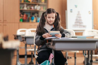 Neşeli bir sınıfta, odaklanmış bir liseli kız masasında oturur, bir kitap okumaya dalmıştır. Mekan renkli dekorasyonlar, eğitim ve keşif ruhuyla dolu..