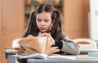 Saçları örgülü, kendini işine adamış bir okul kızı kitabına odaklanmış, çalışmalarına masasında devam ediyor. Sınıf eğitim sıcaklığı ve yaratıcılıkla dolu. Öğrenme deneyimini geliştiriyor..