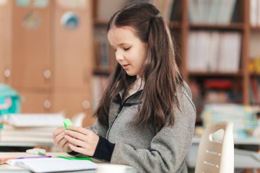 Renkli bir sınıfta, genç bir kız canlı malzemelerle ustalaşmaya dikkatle odaklanır. Eğitimin zevkini kucaklarken masası defterler ve malzemelerle dolu..