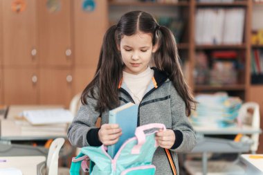Odaklanmış bir ifadeyle, bir öğrenci kitabını dikkatlice parlak renkli bir sırt çantasına koyar..
