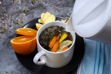 Limonlu, zencefilli, turuncu, reçelli ve koyu gri arka planda tıbbi maskeli beyaz çay. Sağlık hizmetleri. Vitamin kokteyli.