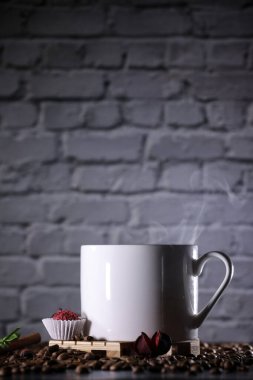 Kahve çekirdeği dolu beyaz bardak, kırmızı çiçekler ve siyah tuğla bir duvarın arkasında kırmızı çikolata şekeri. Sabah espresso. Kahve kupası..