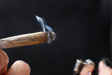 El ele tutuşarak sigara. Siyah arka planda izole edilmiş esrar içmek. Tıbbi kullanım.