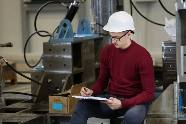 Portrait of a male factory manager in a white hard hat and red sweater Controlling the work process in the helicopter manufacturer.