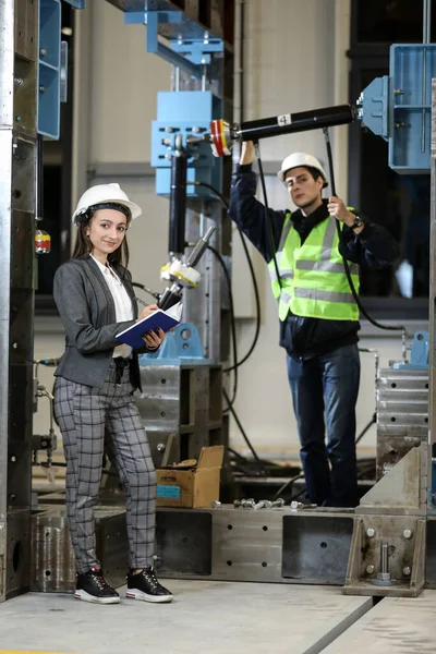 Portrait of a female factory manager in a white hard hat and business suit and factory engineer in work clothes. Controlling the work process in the manufacture.