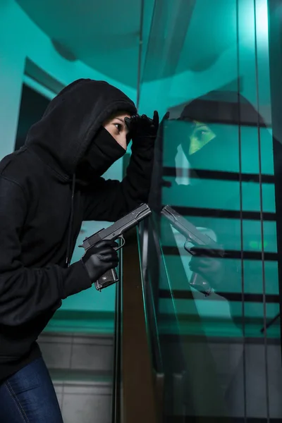 Thief broke into the apartment. House robbery by woman in a black jacket and black mask black gun and crowbar. Burglar in a mask. Thief in a mask trying to break into other people\'s house.