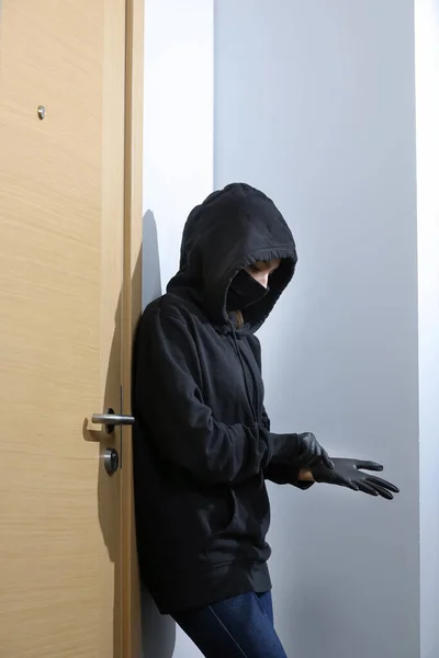 Thief broke into the apartment. House robbery by woman in a black jacket and black mask black gun and crowbar. Burglar in a mask. Thief in a mask trying to break into other people\'s house.