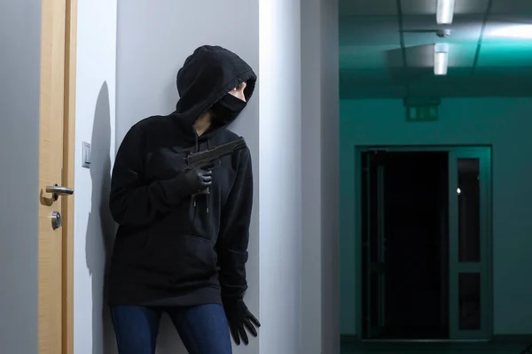 Thief broke into the apartment. House robbery by woman in a black jacket and black mask black gun and crowbar. Burglar in a mask. Thief in a mask trying to break into other people\'s house.