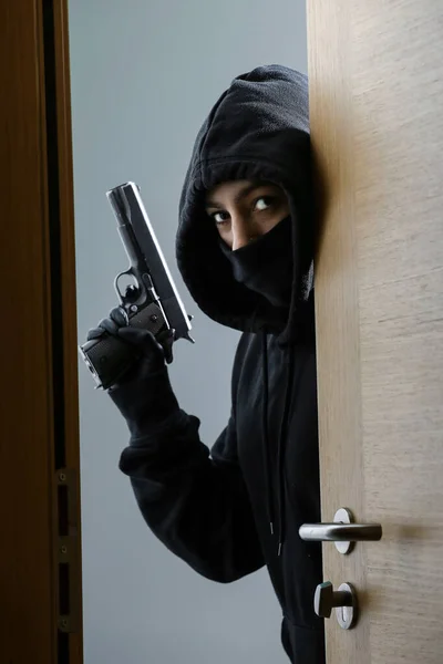 Thief broke into the apartment. House robbery by woman in a black jacket and black mask black gun and crowbar. Burglar in a mask. Thief in a mask trying to break into other people\'s house.