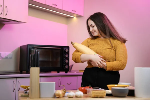 Young woman cooking in a kitchen. Housewife preparing vegetables for cooking. Peel yellow zucchini. Cooking baked zucchini in a oven