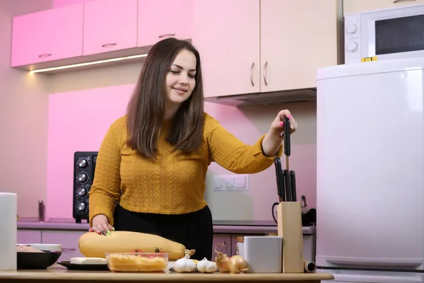 Young woman cooking in a kitchen. Housewife preparing vegetables for cooking. Peel yellow zucchini. Cooking baked zucchini in a oven