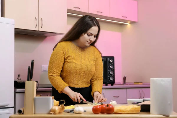 Young woman cooking in a kitchen. Housewife preparing vegetables for cooking. Peel onion. Cooking baked zucchini