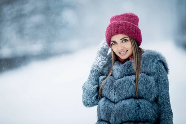 一个穿着灰色皮大衣 头戴红帽子的可爱女孩在雪天行走在冬季森林里的画像 在松林里过冬的心情圣诞节室外时间 — 图库照片