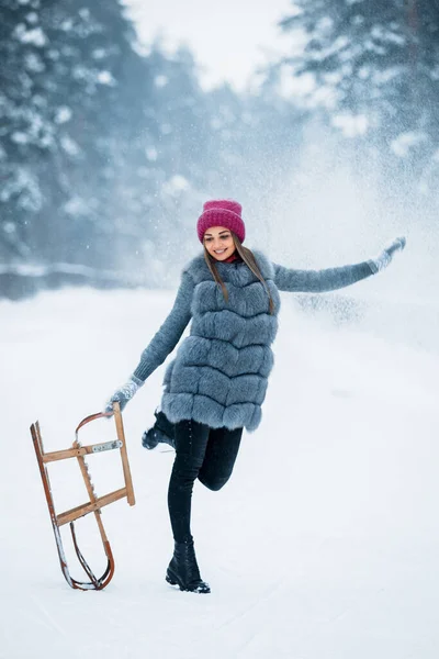 一个穿着灰色毛皮外套 头戴红色帽子的可爱女孩的画像 在雪天里 她站在雪橇上 走在冬季的森林里 冬天的心情圣诞节室外时间 — 图库照片