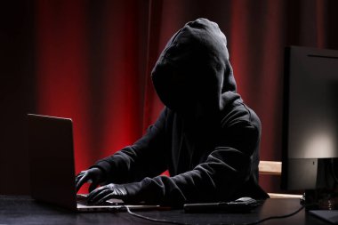 Siyah kazaklı ve siyah maskeli uluslararası hacker siyah ve kırmızı arka planda hükümeti hacklemeye çalışıyor. Siber suçlar. Siber güvenlik.