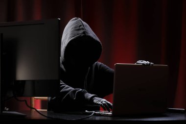 Siyah kazaklı ve siyah maskeli uluslararası hacker siyah ve kırmızı arka planda hükümeti hacklemeye çalışıyor. Siber suçlar. Siber güvenlik.