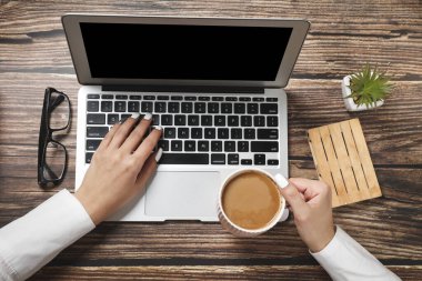 Hippi ahşap çalışma alanı, ofis masası manzarası. Dizüstü bilgisayarda çalışan kadın ellerini düz bir şekilde görüyordum. Ofis işleri. İş toplantısı. Kahve molası.