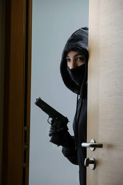 Thief broke into the apartment. House robbery by woman in a black jacket and black mask black gun and crowbar. Burglar in a mask. Thief in a mask trying to break into other people\'s house.