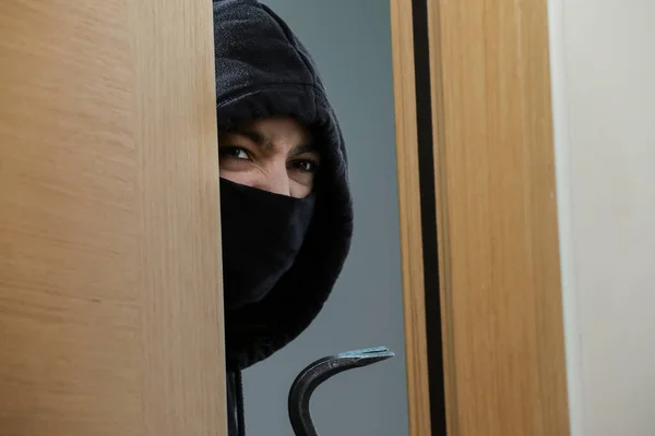 Thief broke into the apartment. House robbery by woman in a black jacket and black mask and crowbar. Burglar in a mask. Thief in a mask trying to break into other people\'s house