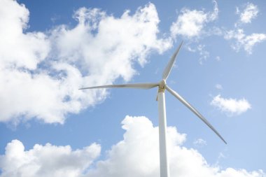 Mavi gökyüzü ve bulutlarla güneşli bir günde rüzgar türbini. Rüzgâr tarlası eko alanı. Yeşil ekolojik enerji üretimi.