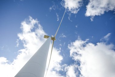 Mavi gökyüzü ve bulutlarla güneşli bir günde rüzgar türbini. Rüzgâr tarlası eko alanı. Yeşil ekolojik enerji üretimi.