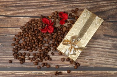 Kahve çekirdekleri, kırmızı çiçekler ve ahşap arka planda altın hediye kutusu. Sevgililer Günü.