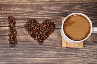 Kalp şeklinde kahve çekirdekleri ve ahşap arka planda beyaz kahve kupası. Kahve severler..