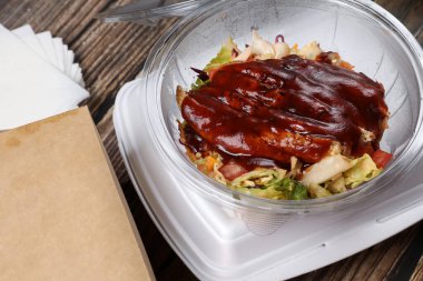 Tahta bir masada plastik bir kabın içinde BBC tavuklu salatanın üst görüntüsü. İş yemeği. Eve ve ofise yemek teslimatı.