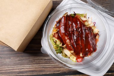 Tahta bir masada plastik bir kabın içinde BBC tavuklu salatanın üst görüntüsü. İş yemeği. Eve ve ofise yemek teslimatı.