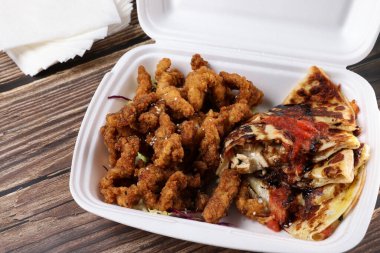 Plastik kaplarda yiyecek dolu bir masa. Yemek servisi. Tavuk salatası, pizza, soslu tavuk kanadı, ahşap masada hamburger ve patates kızartması. İş yemeği..