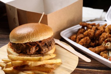 Plastik kaplarda yiyecek dolu bir masa. Yemek servisi. Tavuk salatası, soslu tavuk kanadı, ahşap masada patates kızartması üzerine hamburger. İş yemeği..