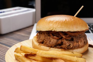  Siyah arka planda dizüstü bilgisayarın önünde patates kızartması ve taze pişmiş sığır burger. Eve yemek servisi..