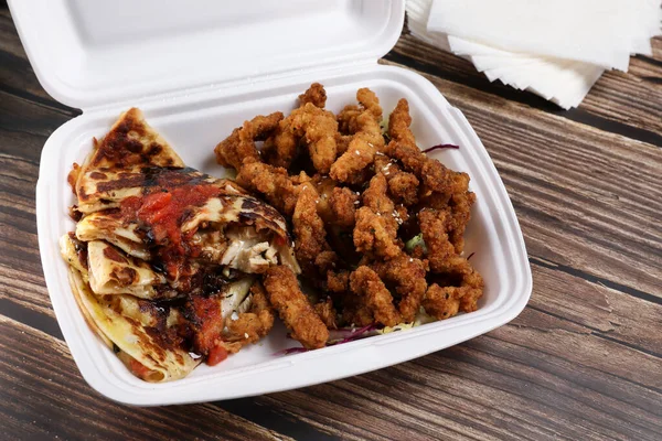 Plastik kaplarda yiyecek dolu bir masa. Yemek servisi. Tavuk salatası, pizza, soslu tavuk kanadı, ahşap masada hamburger ve patates kızartması. İş yemeği..