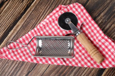 Pizza bıçağı ve peynir rendesi beyaz ve kırmızı peçeteyle ahşap bir masada. Pizza pişiriyorum..