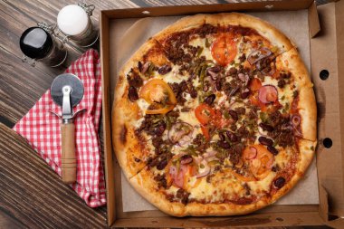 Karton bir kutuda taze pişmiş pizza peçetede pizza bıçağı, ahşap bir masada tuz ve biber. Pizza teslimatı Evde ye..