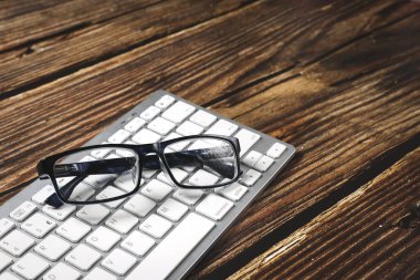 Beyaz klavyenin üst görüntüsü ve ahşap bir masanın üzerindeki siyah gözlükler. Uzayı kopyala İş toplantısı. Ofis işi.