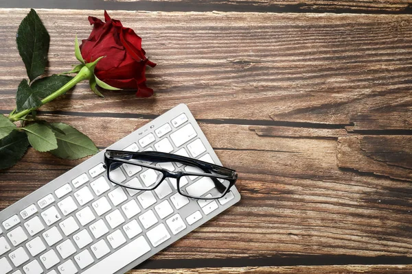 Top view of white keyboard , red rose and black glasses on a wooden table. Copy space. Business meeting. Office work.
