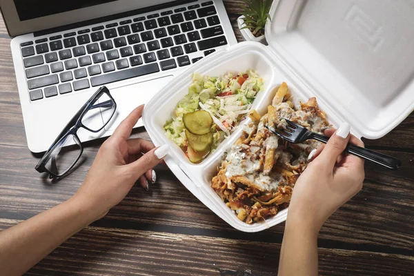 Kadın elleri dizüstü bilgisayarın yanındaki tahta masada yemek kabını açıyor. Fast food teslimatı. Evde iş yemeği yiyorum. Evden çalışıyorum. Uzak çalışma