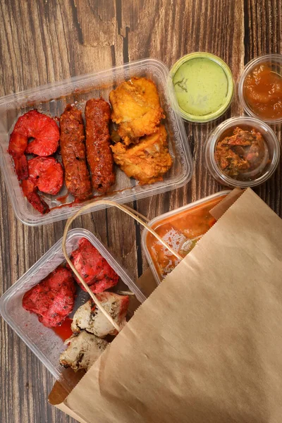 Top view of traditional Indian food in a plastic box on a wooden table. Indian fast food delivery at home. Eat at home.