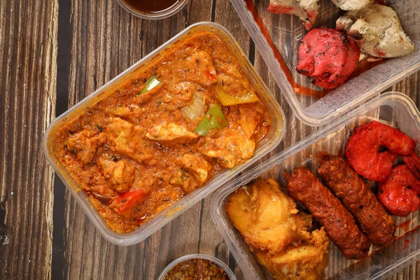 Top view of traditional Indian food in a plastic box on a wooden table. Indian fast food delivery at home. Eat at home.