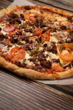 Tahta bir masada taze pişmiş et ve sebzeli pizza manzarası. Pizza teslimatı Götürün..