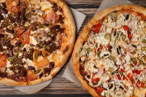 Ahşap bir masada et, mantar ve sebzeli iki taze pizza. Pizza teslimatı Götürün..