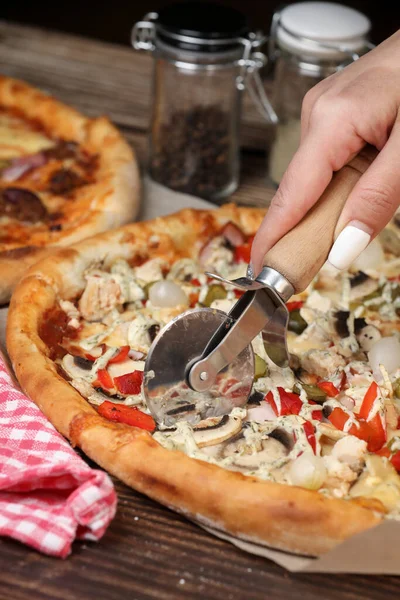 woman\'s hand cuts the pizza with a pizza knife. Home made pizza. Home delivery.