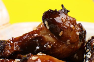 Sarı arka planda izole edilmiş plastik bir kabın içinde taze pişmiş lezzetli tavuk kanatları. Yemek teslimatı.