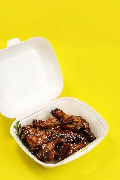 黄色の背景に隔離されたプラスチック容器で新鮮な調理おいしい鶏の羽 食品の配達 — ストック写真
