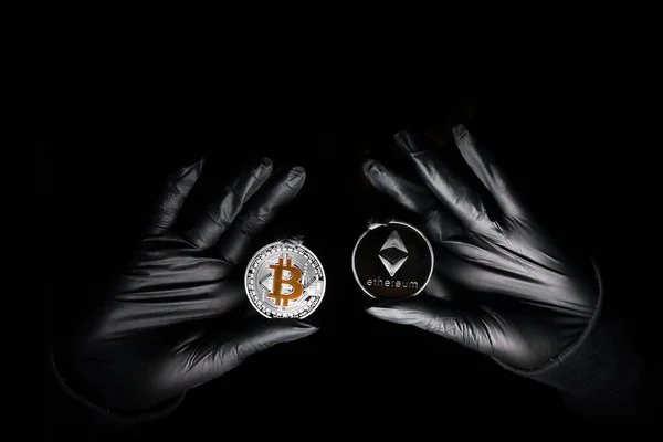 Siyah arka planda Bitcoin ve Ethereum madeni para tutan siyah eldivenler. Uluslararası hacker şifreli para birimlerinizi çalmaya çalışıyor. Zincirleme güvenlik.